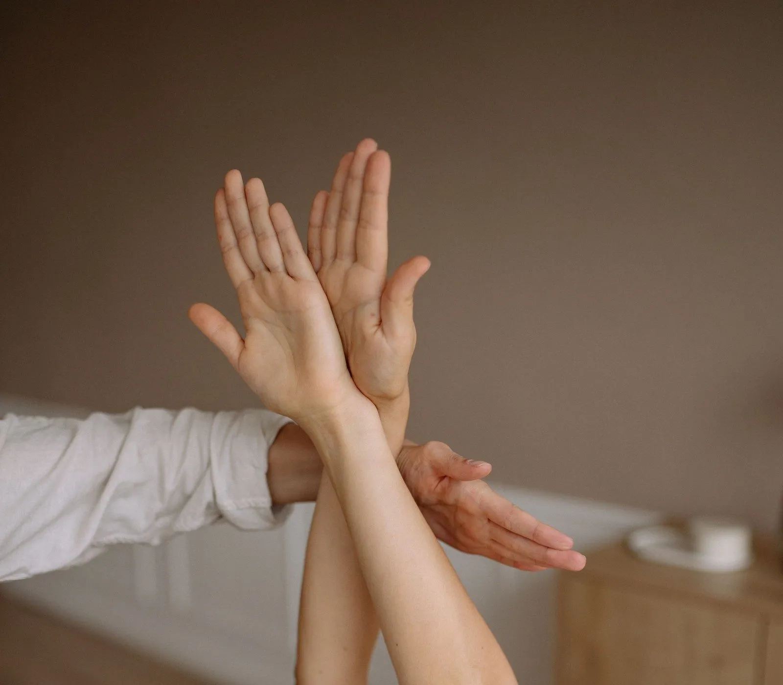 A patient lying on a treatment table reaches both arms straight up while a therapist guides the movement