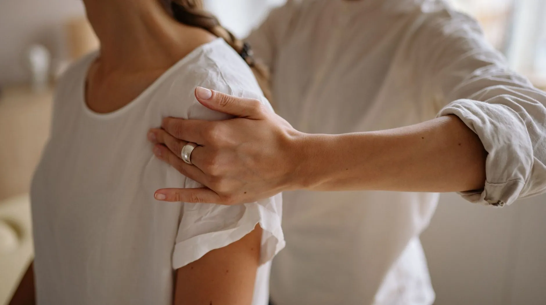 A therapist's hand rests on the front of a patient's shoulder to guide her posture