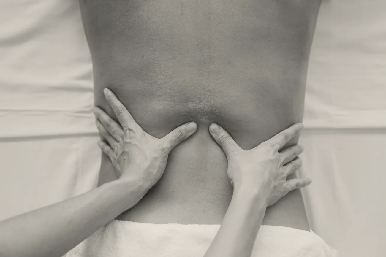 A therapist's hands working the muscles of a patient's lower back